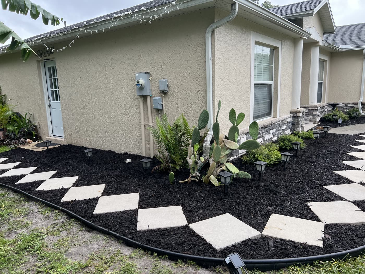 Black mulch bed with agave and stepping stones along a North Port house