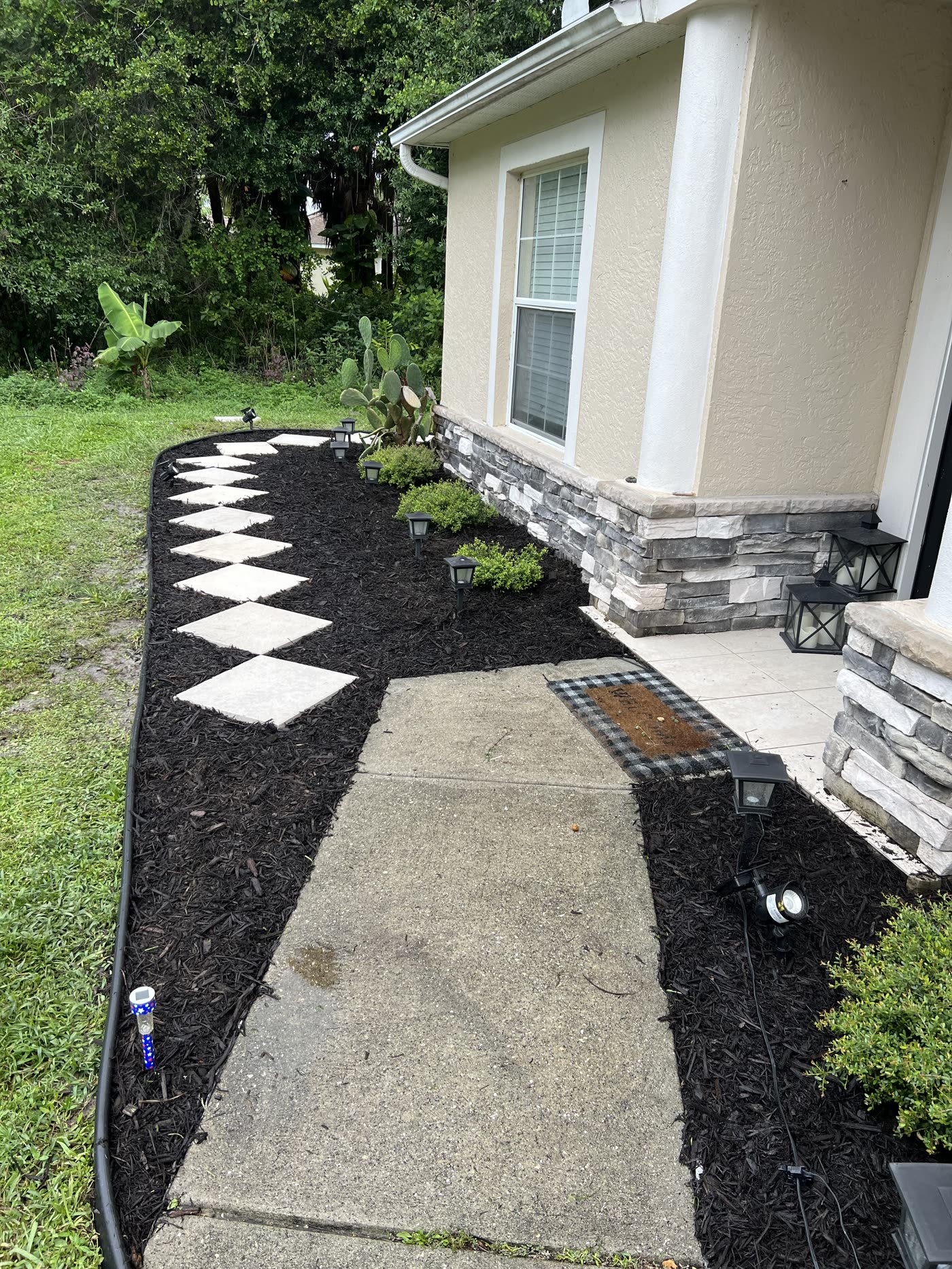 Checkerboard stepping stones in a fresh mulch bed by a stone-veneer entry